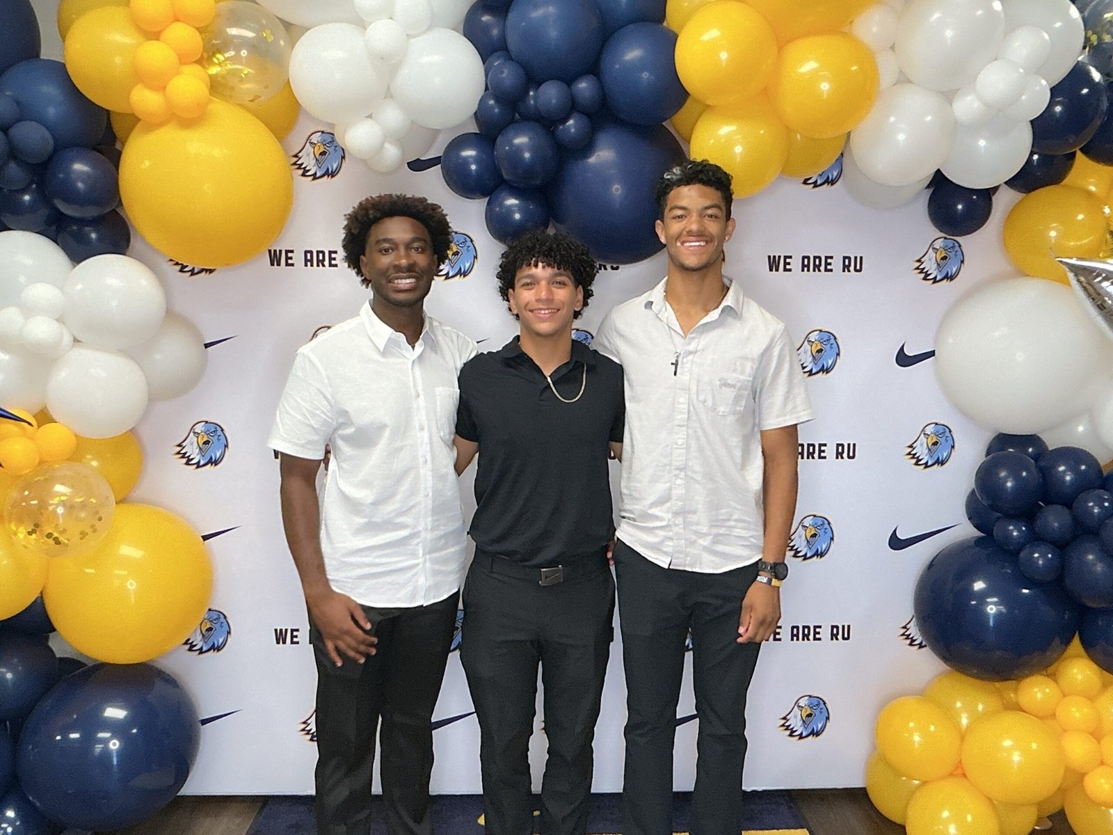 Three awards-night guests beneath navy, gold and white balloons