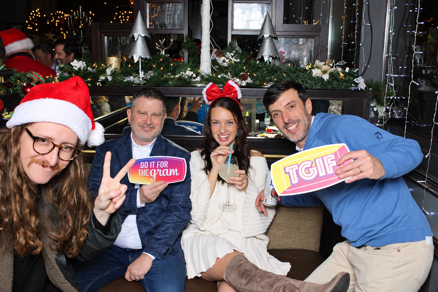 Four company holiday party guests laughing with festive hats and playful signs